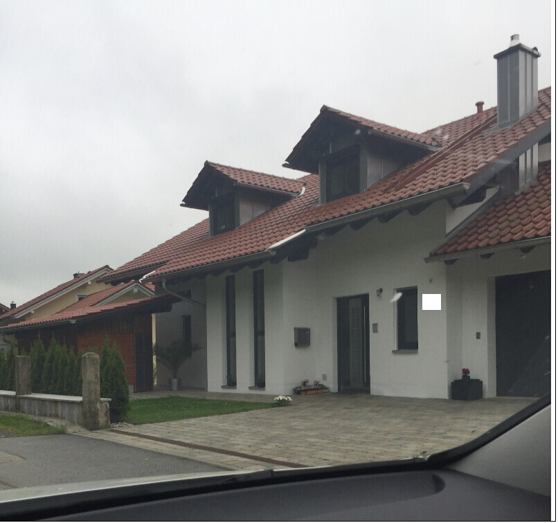 Modernes Reihenhaus mit roten Ziegeldächern, weiße Fassade, gepflasterte Einfahrt, Blick aus Auto