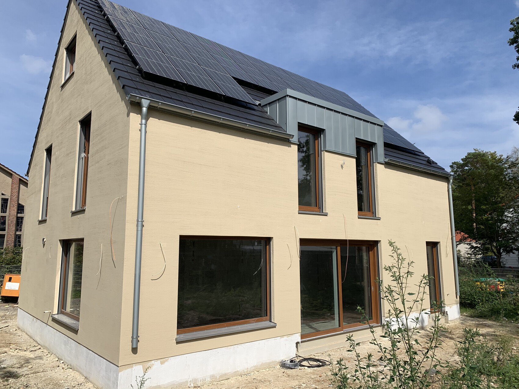 Modernes zweistöckiges Haus mit Solarmodule auf dem Dach, große Fensterfronten und beige Fassade.