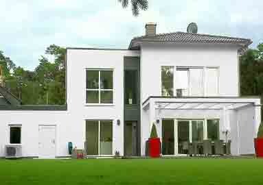 Moderne weiße Hausfassade mit Terrasse, Glasfront und grünem Rasen.