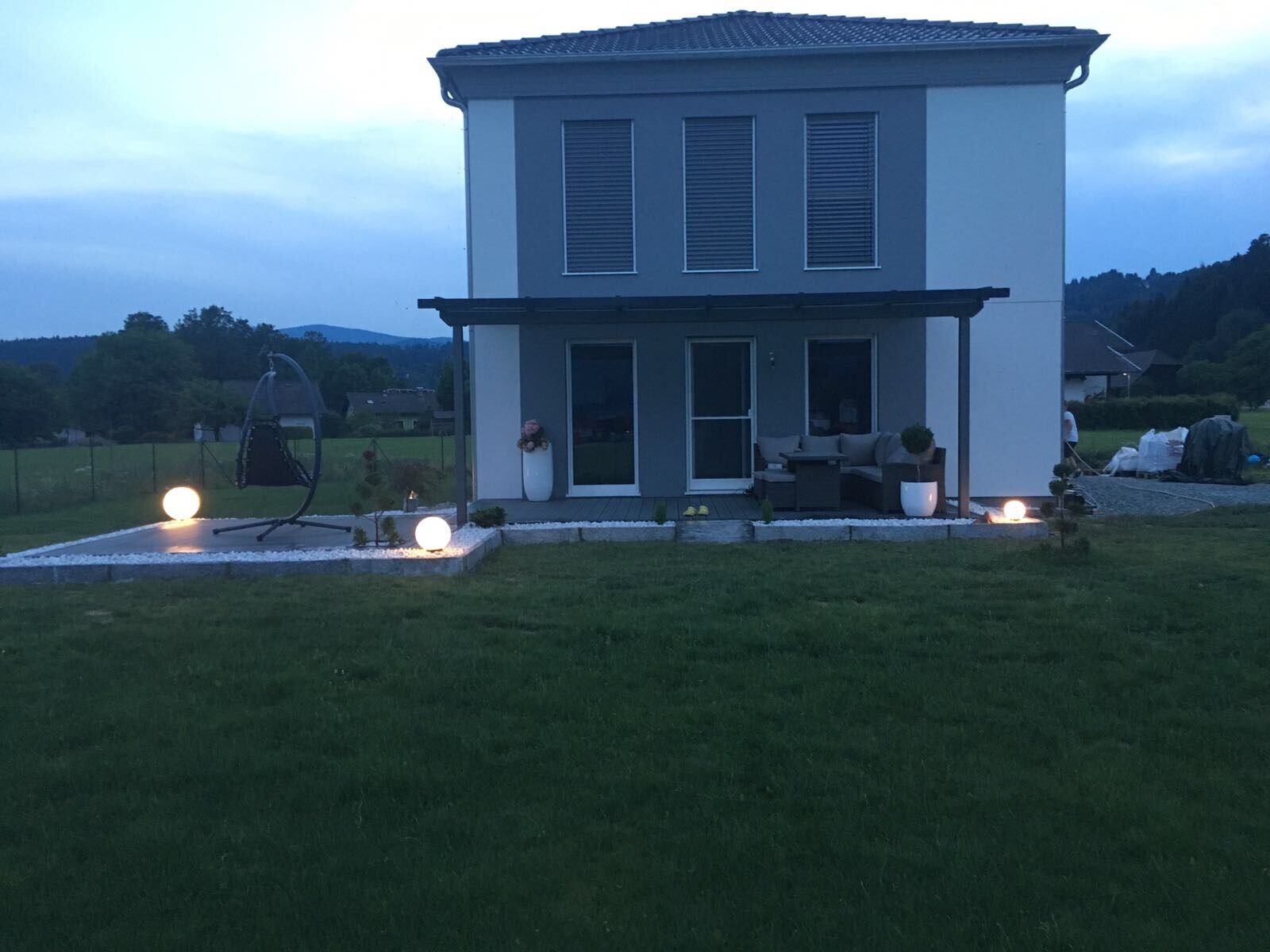 Zweistöckiges modernes Haus mit Terrasse, Hängesessel, Lounge-Möbeln und Gartenbeleuchtung.