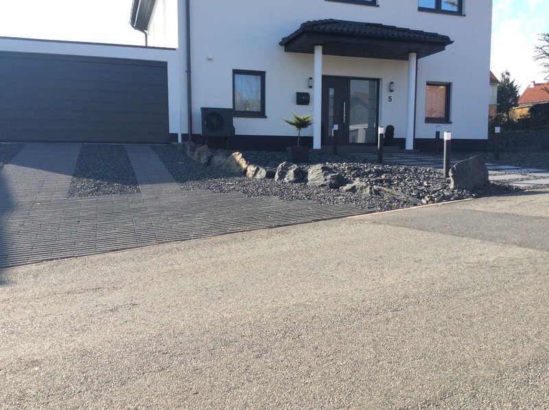 Moderne weiße Wohnhausfront mit dunkler Eingangstür, gepflastertem Weg und Kiesstreifen.