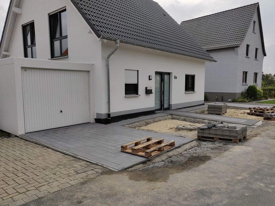 Moderne Hausfront mit Garage, Eingangstür und gepflastertem Vorplatz.