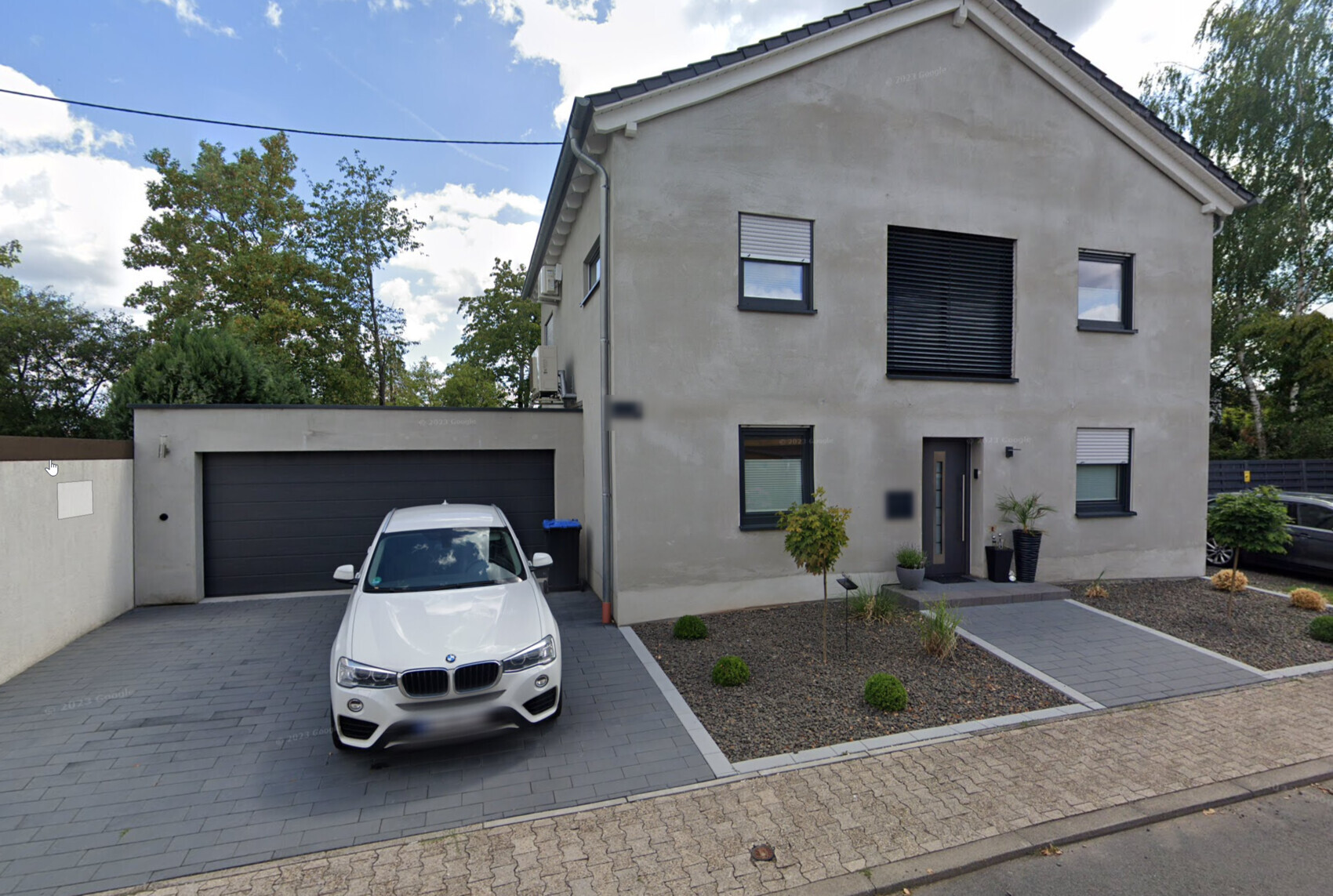 Moderne zweigeschossige Hausfront mit Garage, weißem BMW davor, Gartenfläche.
