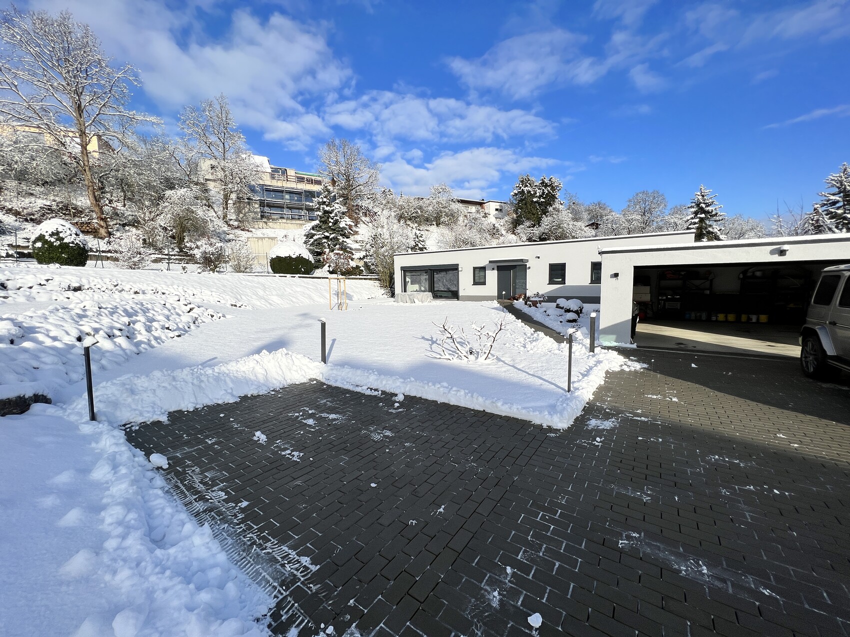 Moderne Garage mit offener Tür, verschneiter Hof und Van davor; blauer Himmel im Winter.