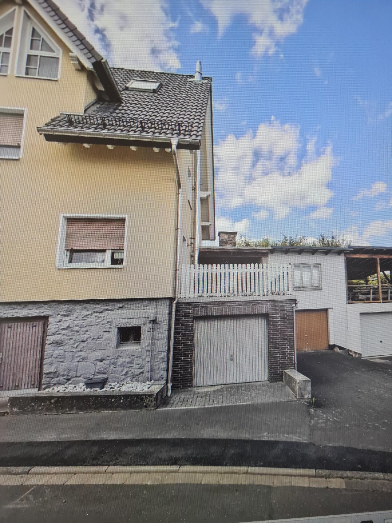 Zweigeschossiges Wohnhaus mit Garage, Steinunterbau, beige Fassade und Dachziegeln.