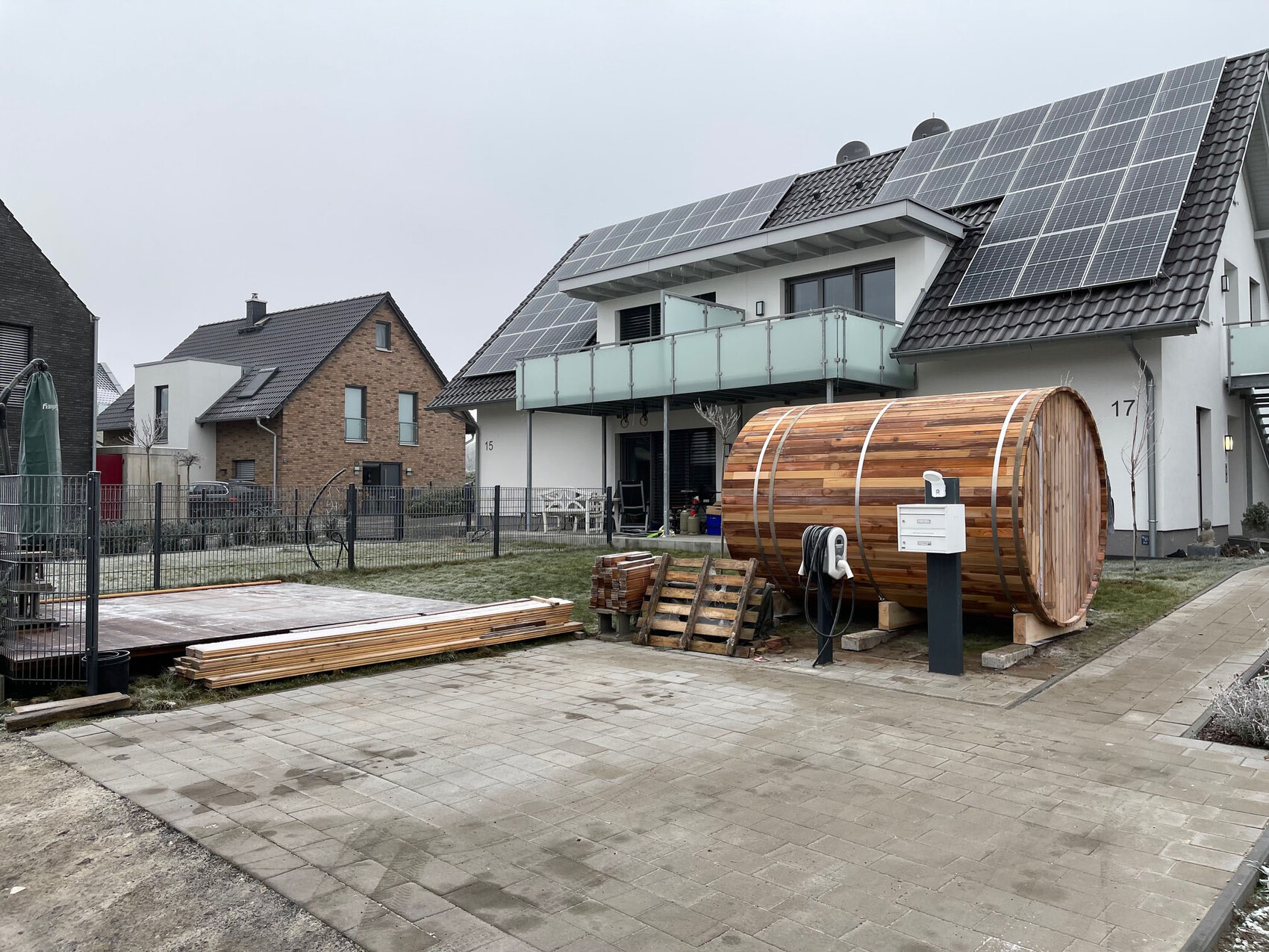 Große Holzfass-Sauna neben Wohnhaus mit Solarplatten auf dem Dach.