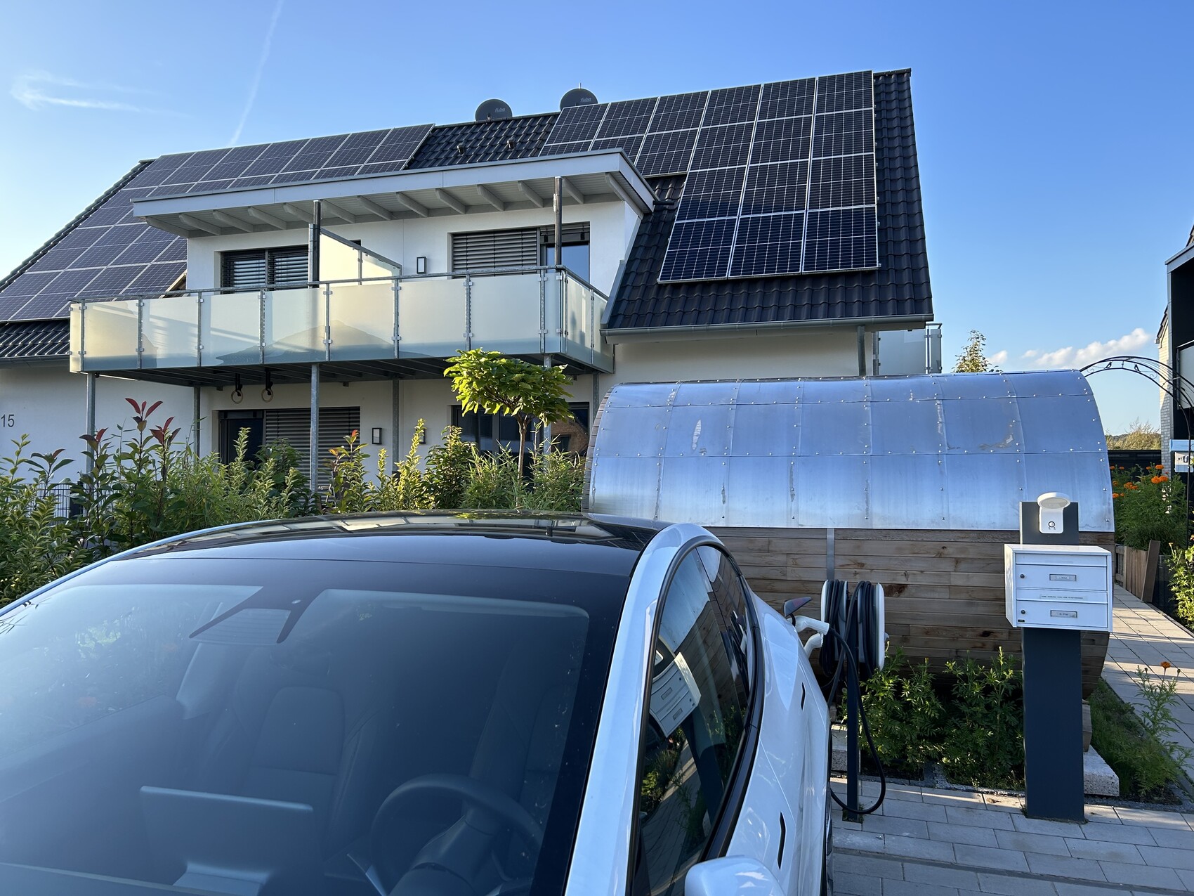 Modernes Einfamilienhaus mit Solar-Dach, Glasbalustrade und davor geparktes Auto.