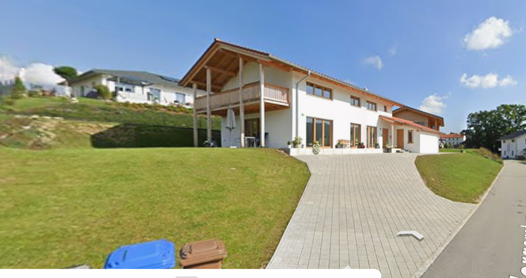 Moderne weiße Hausfront mit Terrasse, großen Fenstern und grünem Garten.