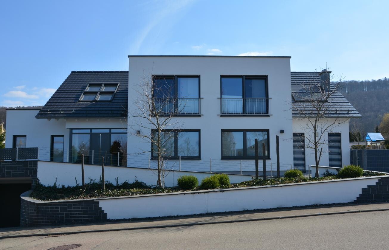 Moderne weiße Villa mit zwei Etagen, großen Fenstern, Balkonen und Garten vorne.