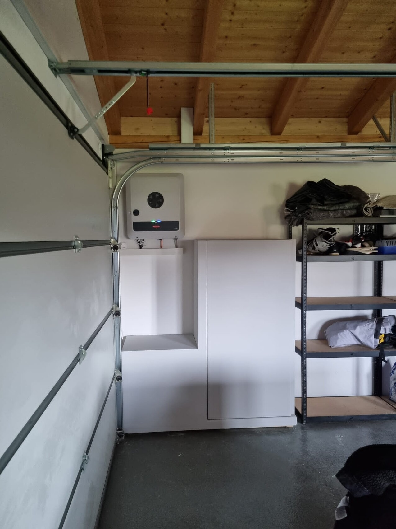 Weißes Heizgerät an der Wand, daneben ein weißer Schrank; Metallregal mit Kleidung in der Garage.