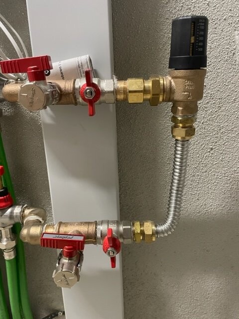 Wandmontierte Wasserleitung mit roten Kugelhähnen, Mess-/Druckregler und Flex-Schlauch