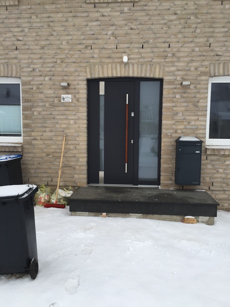 Schwarze Haustür in Backsteinfassade, vertikaler Holzstreifen, Treppe, Schnee; Briefkasten rechts