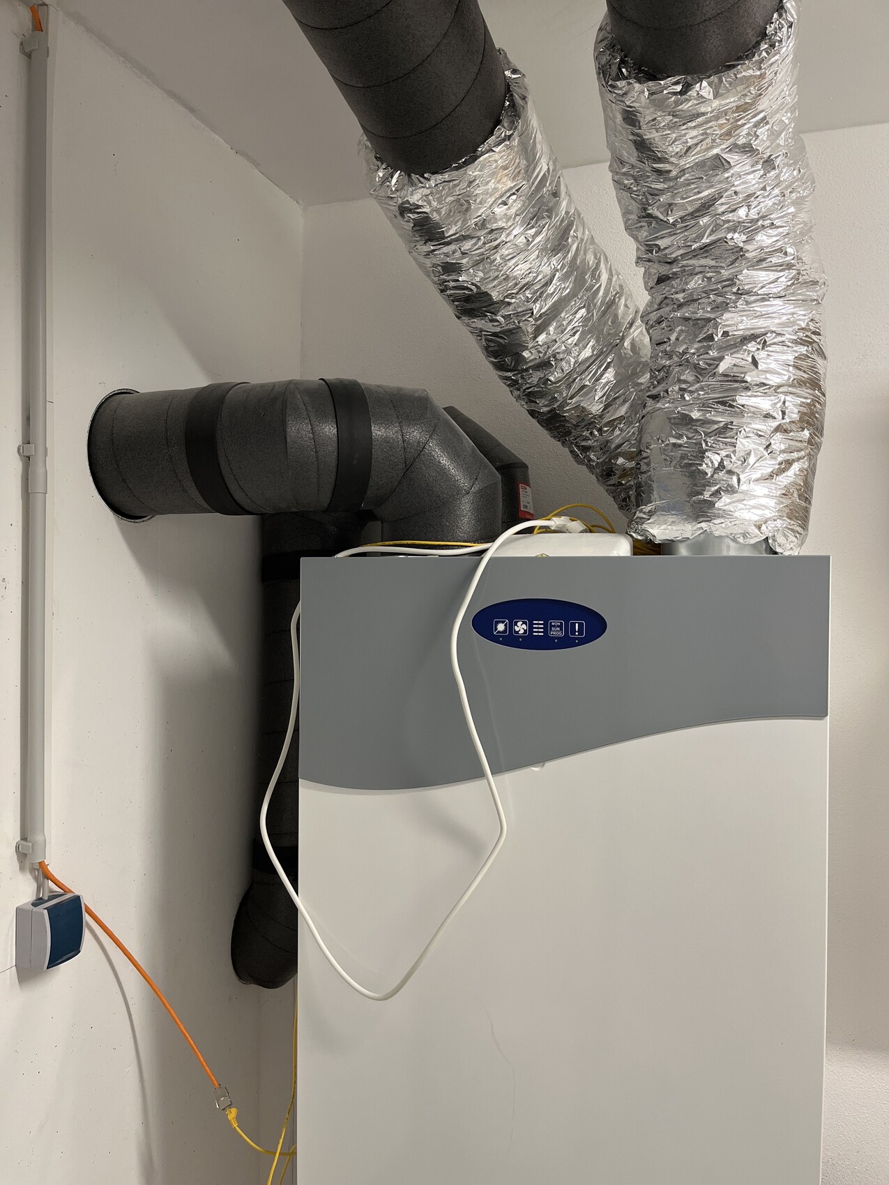 Kellerraum mit Heizungs- und Lüftungsanlage, isolierten Rohren und Steuerpanel.