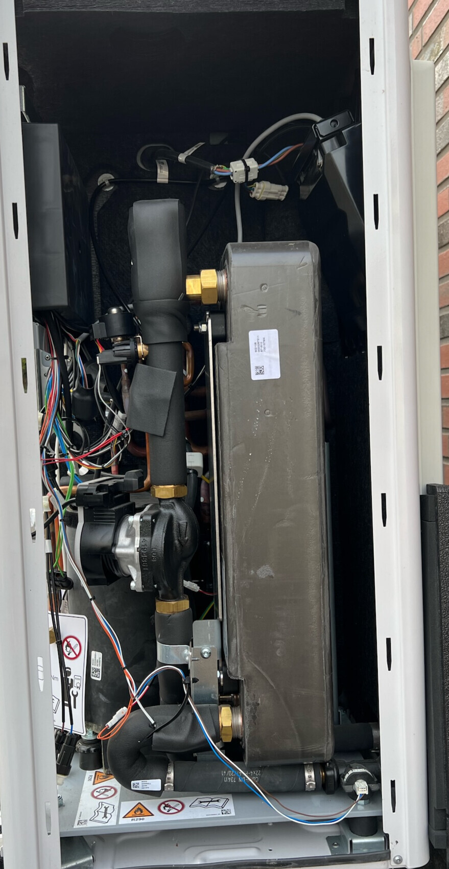 Innenansicht einer Heizungsanlage im Schaltschrank mit Pumpe, Wärmetauscher und Rohren.