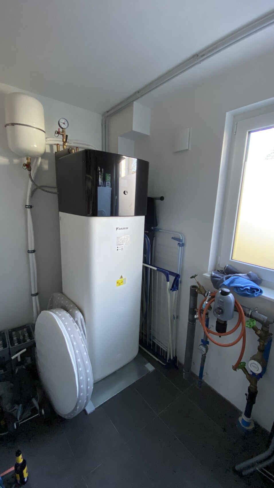 Technikraum mit Daikin Warmwasserboiler, Ausdehnungsgefäß, Rohren und Fenster.