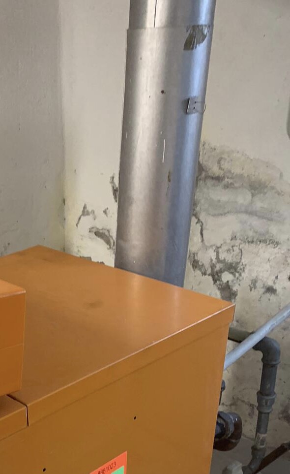 Orangener Heizkessel mit Metallrohr im Kellerraum.