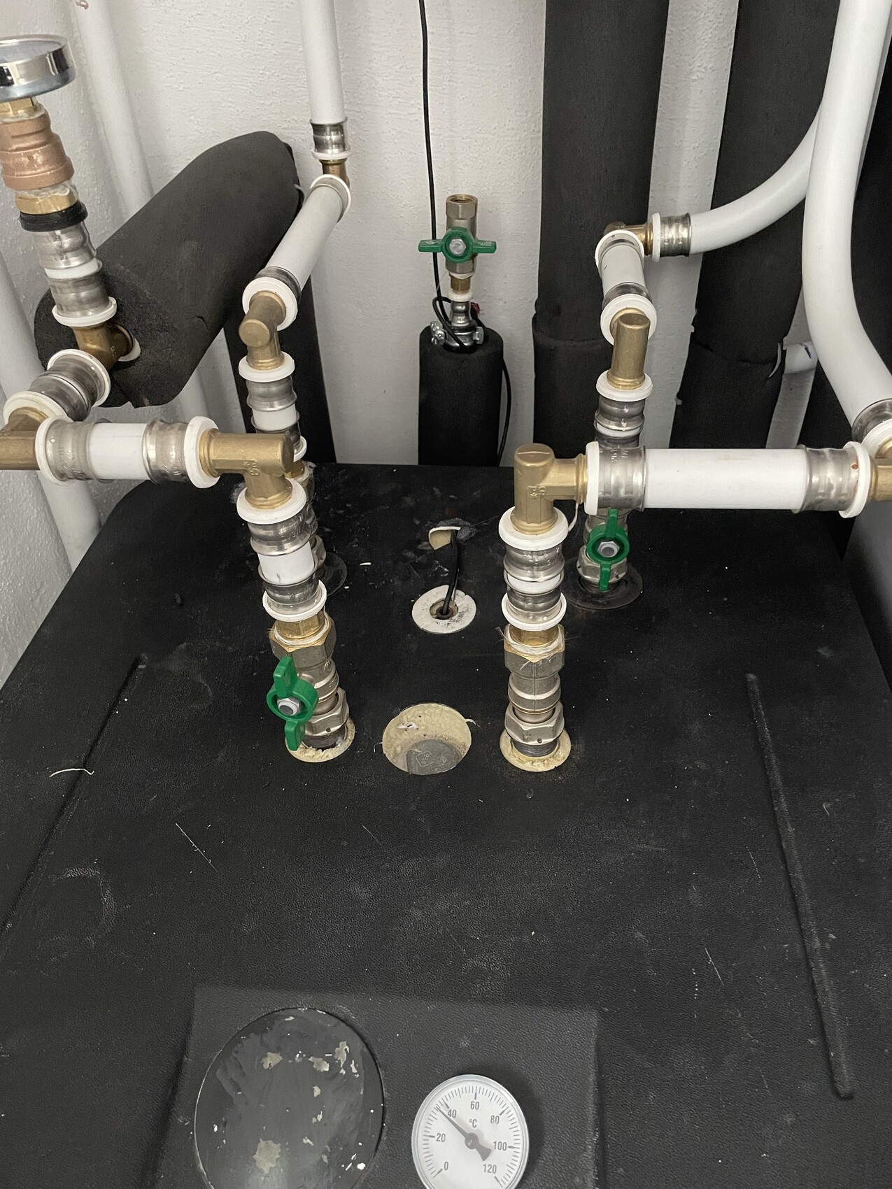 Wasserleitungen mit PVC-Rohren, Messingfittings, grünen Absperrventilen und Druckmessgerät.