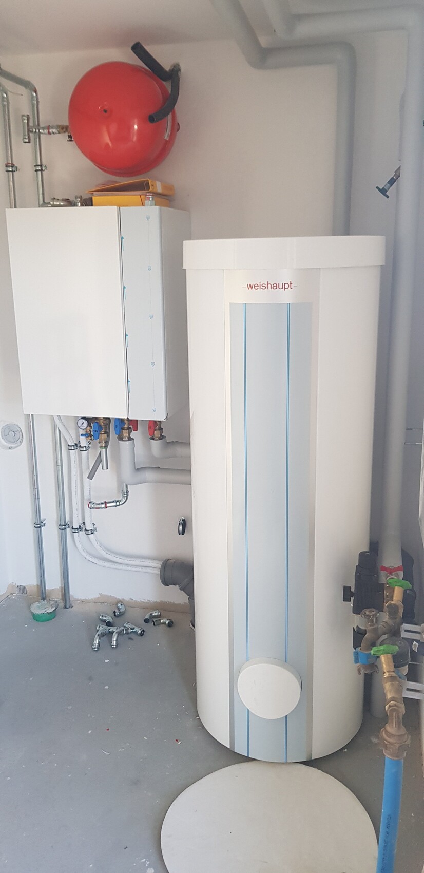 Weißer Heizkessel mit Speichertank, rotem Ausdehnungsgefäß und Leitungen im Technikraum