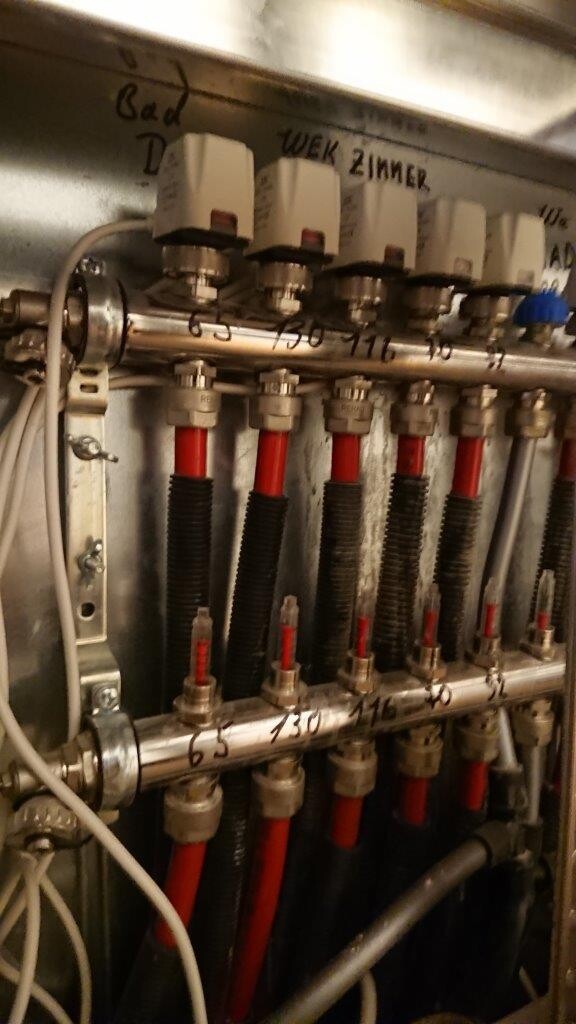 Heizungs- und Hydraulik-Verrohrung: Metallrohre, rote Schläuche, Ventile mit weißen Griffen.