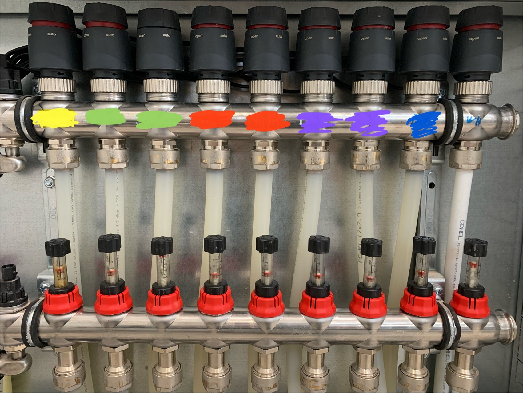 Edelstahl-Verteiler mit farbigen Markierungen Gelb, Grün, Orange, Lila, Blau und roten Ventilkappen.