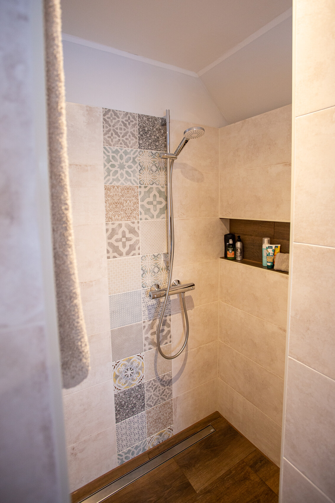 Dusche mit bunter Patchwork-Tile-Wand, Handbrause und Ablage mit Pflegeprodukten.