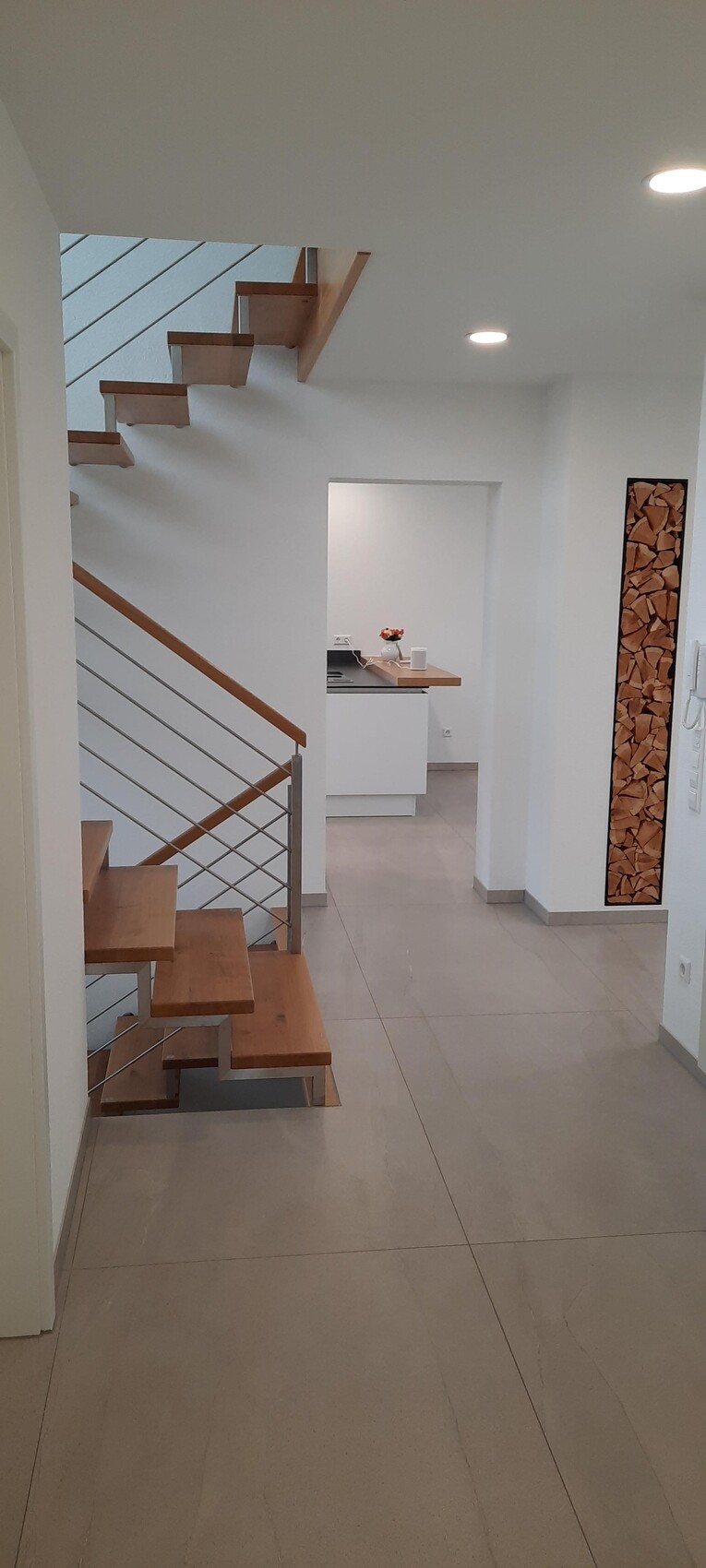 Moderne Innenansicht: offener Flur mit Holzstufen und Küche im Hintergrund.