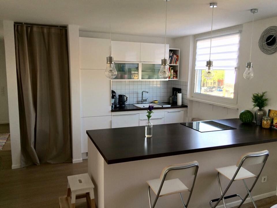 Moderne Küche mit dunkler Insel, weiße Schränke, Pendelleuchten, Spüle am Fenster, Vase mit Blume.