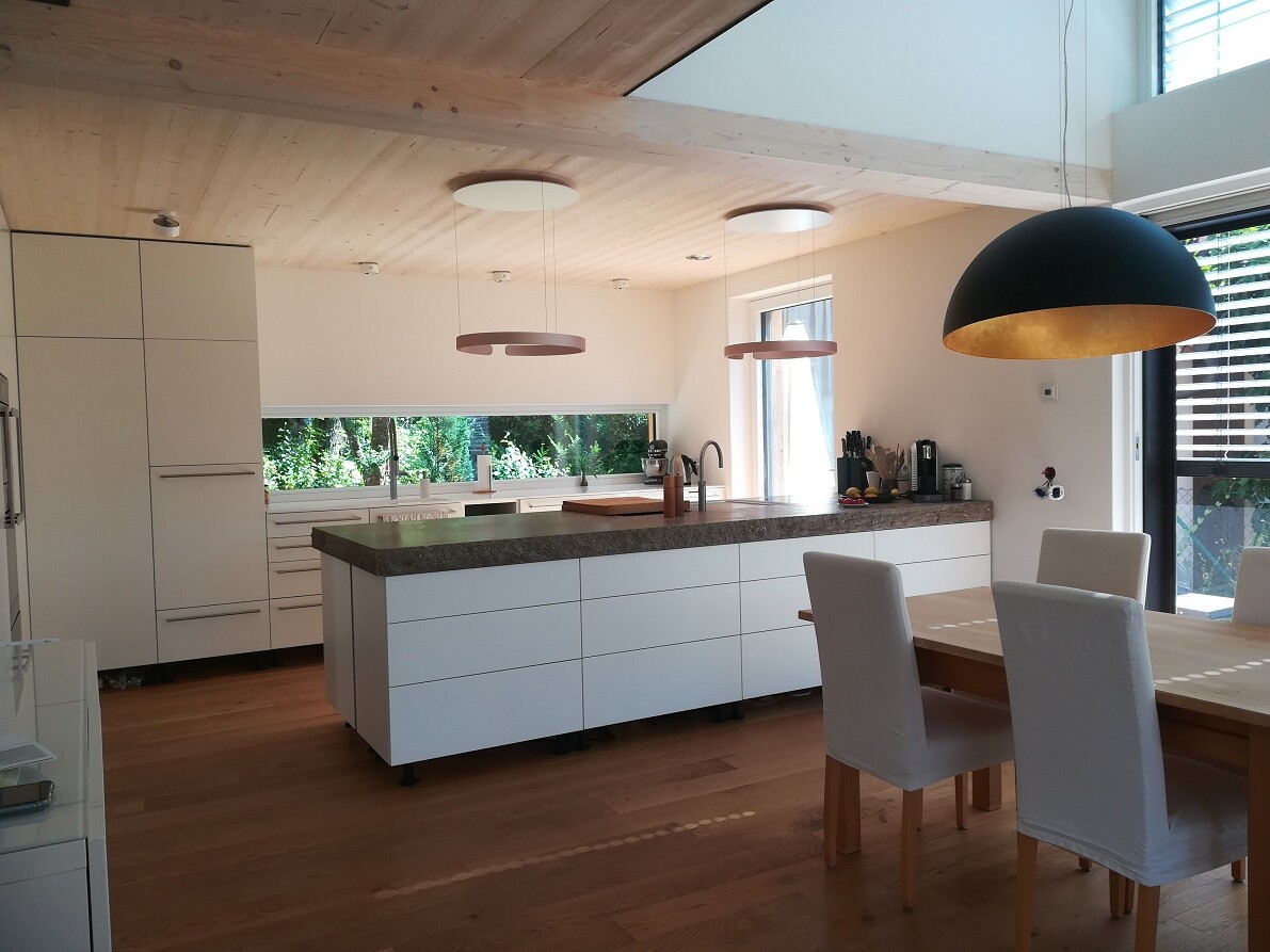 Moderne Küche mit weißer Insel, Holzbalkendecke, Esstisch und großen schwarzen Pendellampen.