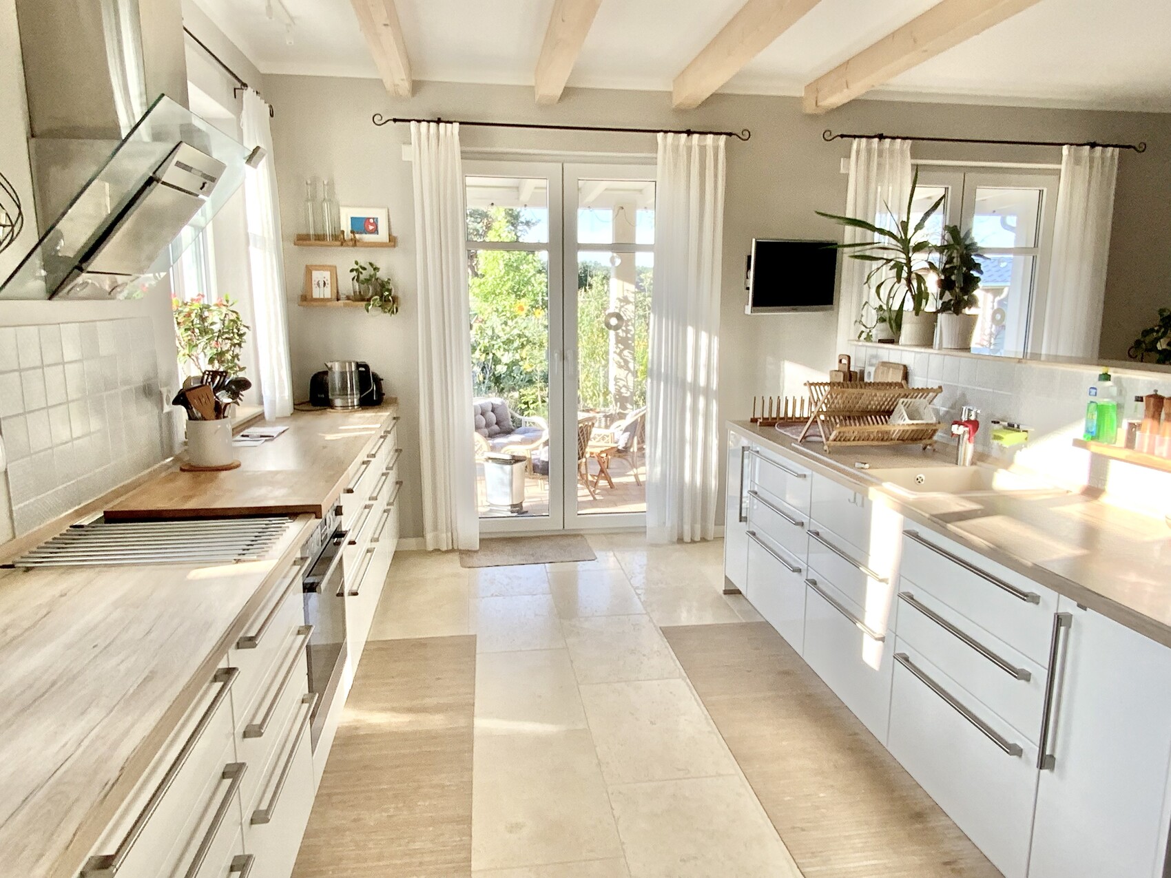 Helle Küche mit weißen Schränken, Insel, Dunstabzug, Glas-Türen zur Terrasse und Garten.