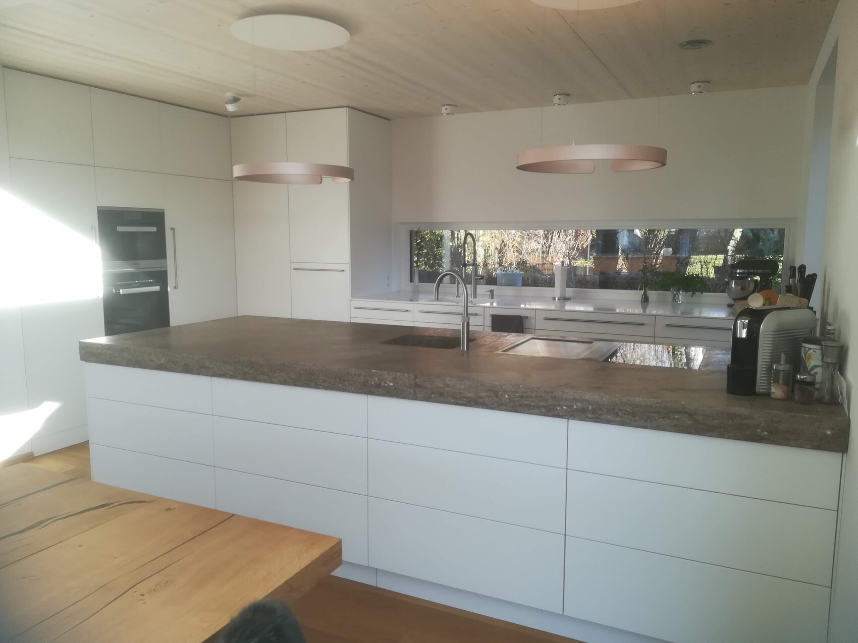 Moderne weiße Küche mit Insel, Spüle, Ofen und Kaffeemaschine; Fensterblick.