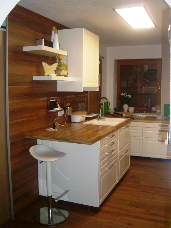 Moderne Küche mit Holzwand, weißer Insel, Barhocker, Spüle und Fenster mit Blumenkasten.