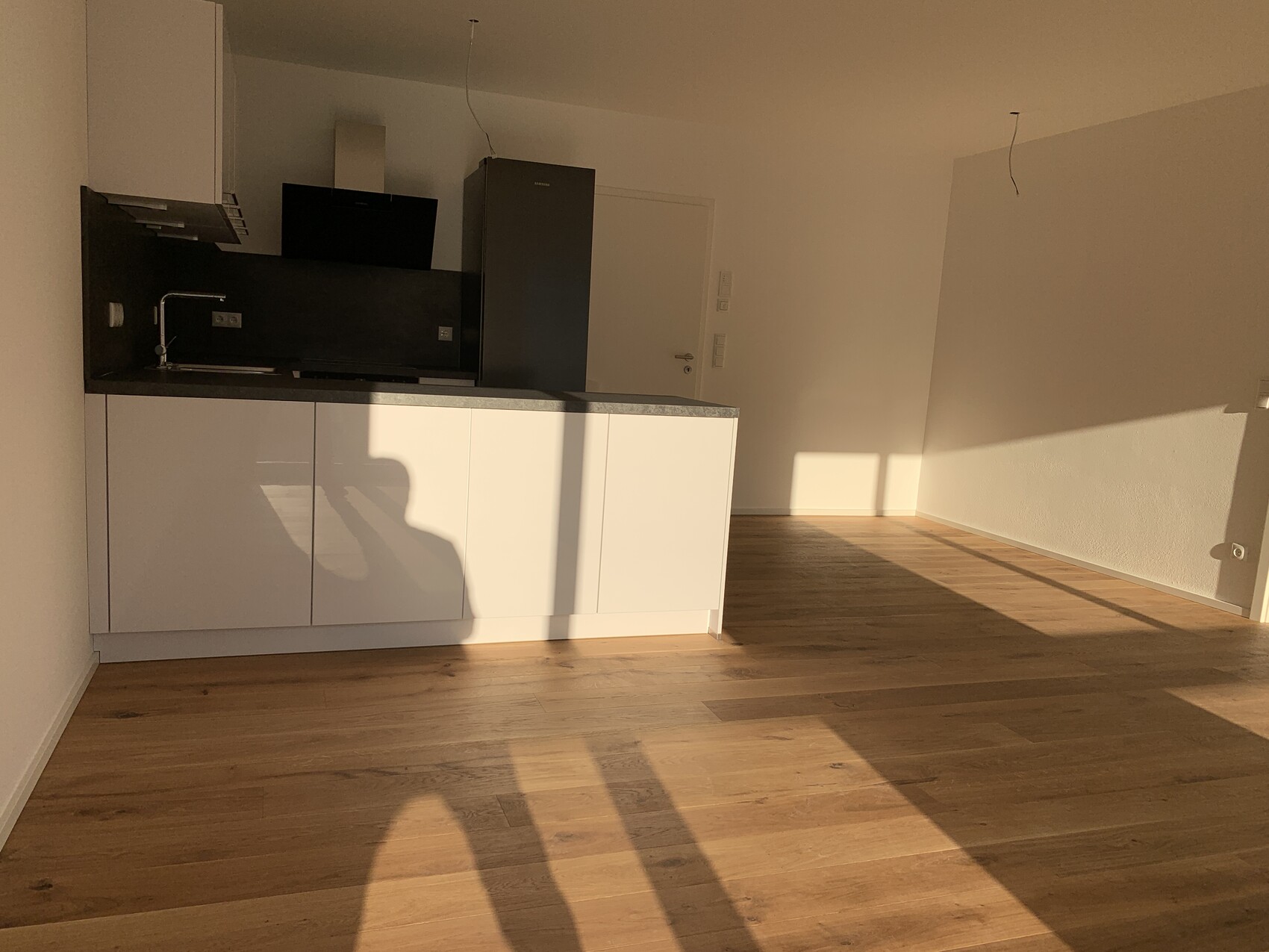 Moderne leere Küche mit weißen Schränken, dunkler Arbeitsplatte, Insel, Holzfußboden, Sonnenlicht.