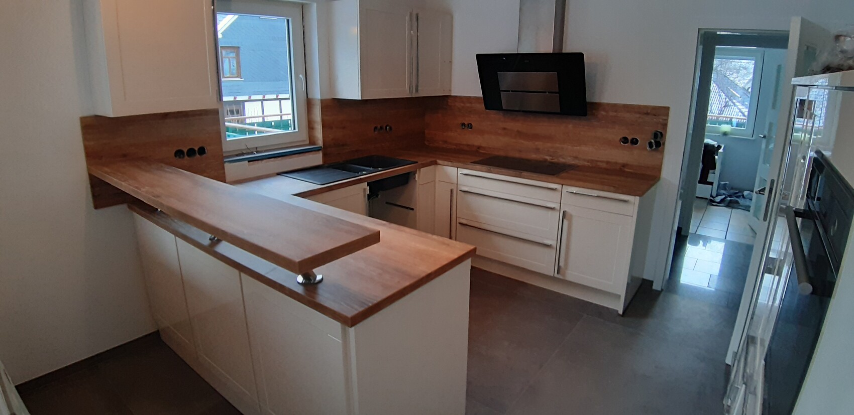Moderne Küche: weiße Schränke, Holz-Arbeitsplatten, Insel, Kochfeld, Dunstabzug und Fenster.