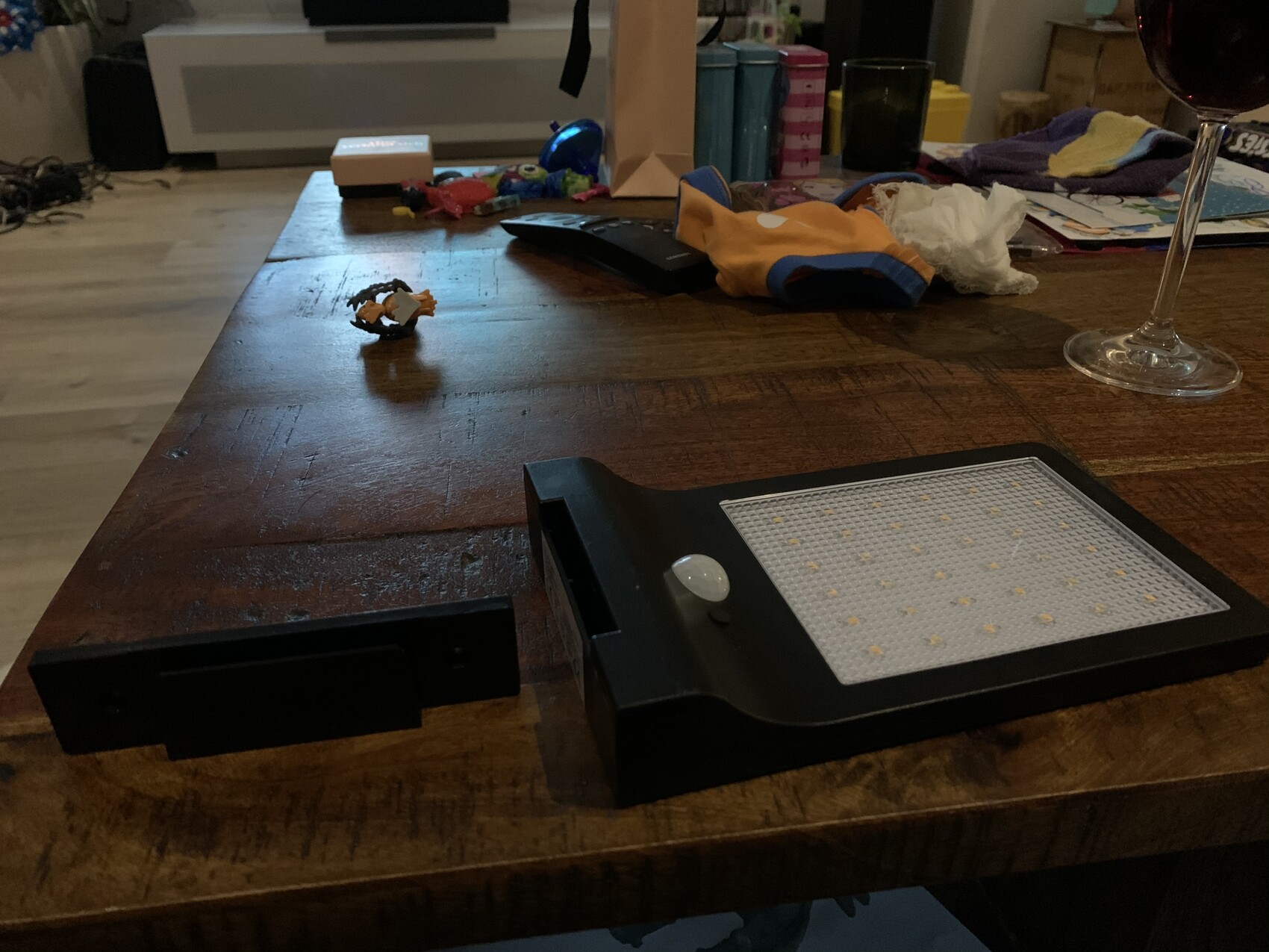 Ein LED-Lichtpanel liegt auf einem Holztisch; rechts ein Weinglas, links Kleinteile verstreut.