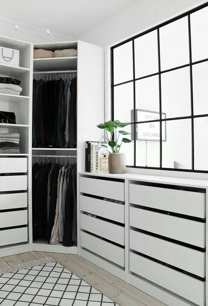 Offenes weißes Kleiderschrank-System mit Kleiderstange, Kommode, Pflanze und großem Gitterfenster.