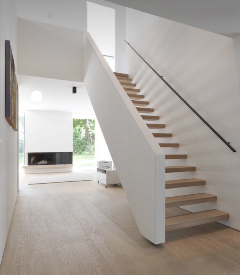 Helles Wohnzimmer mit moderner, offener Holztreppe, Kamin und großen Fenstern im Hintergrund.