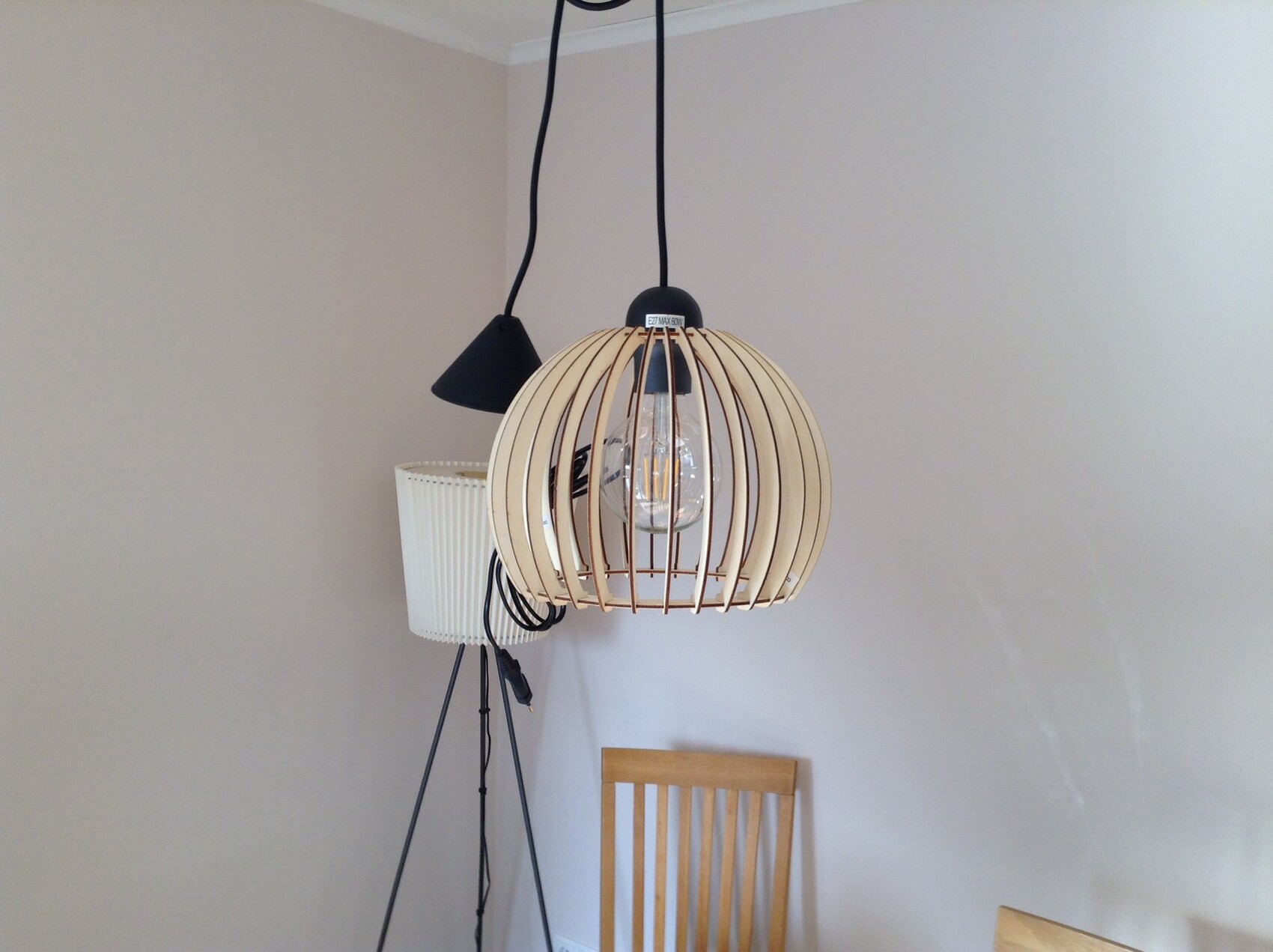 Pendellampe aus Holzlamellen, kugelförmig um Glühbirne; daneben Bodenlampe und Stuhl.