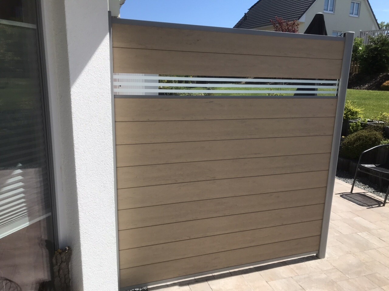 Sichtschutzwand aus Holzpaneelen mit Glasstreifen auf der Terrasse, Gartenblick.