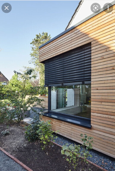 Modernes Holzhaus mit großer Fensterfront, schwarzem Rollladen und Garten davor.