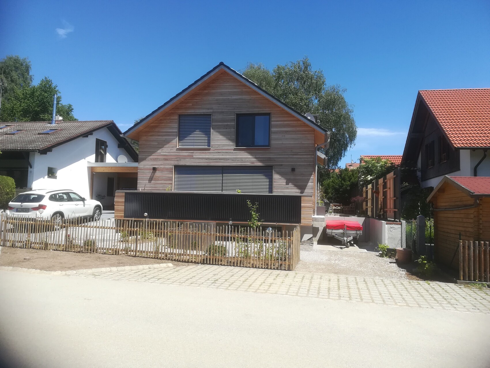 Holzhaus in Vorstadt mit Holzverkleidung, Auto links, Bootanhänger mit roter Abdeckung rechts.