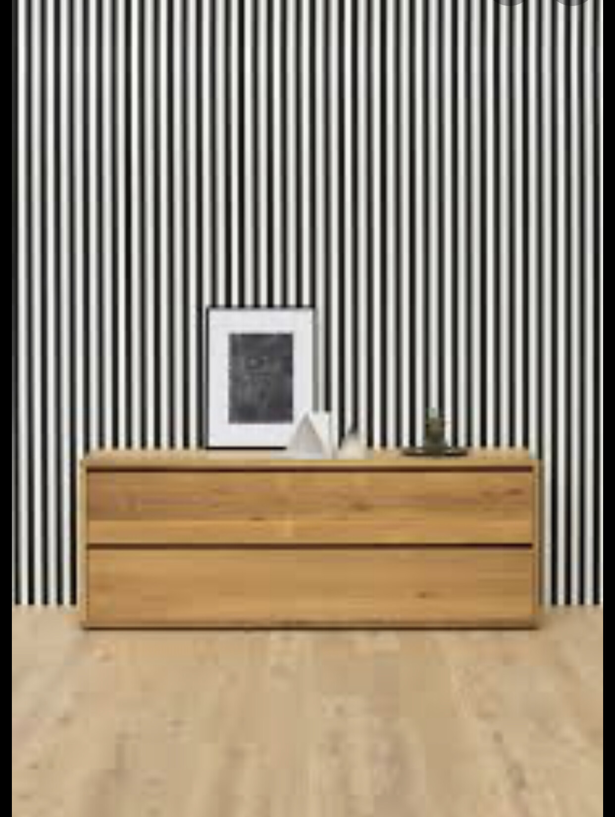 Holzsideboard vor schwarz-weißer Streifenwand; Bilderrahmen, Taschentuchbox, kleines Gefäß darauf.
