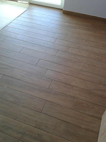 Brauner Holzlaminatboden mit rechteckigen Platten in einem Zimmer; Türöffnung im Hintergrund.