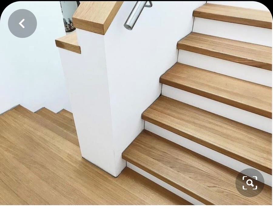 Innenstiege mit Holzstufen, weißen Wänden und einer zentralen Wand zwischen zwei Treppenläufen.