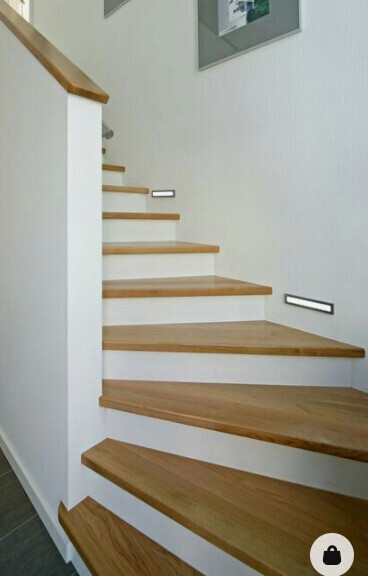Innenansicht einer Holztreppe mit hellbraunen Stufen, weißen Seitenwangen und Wandleuchten.