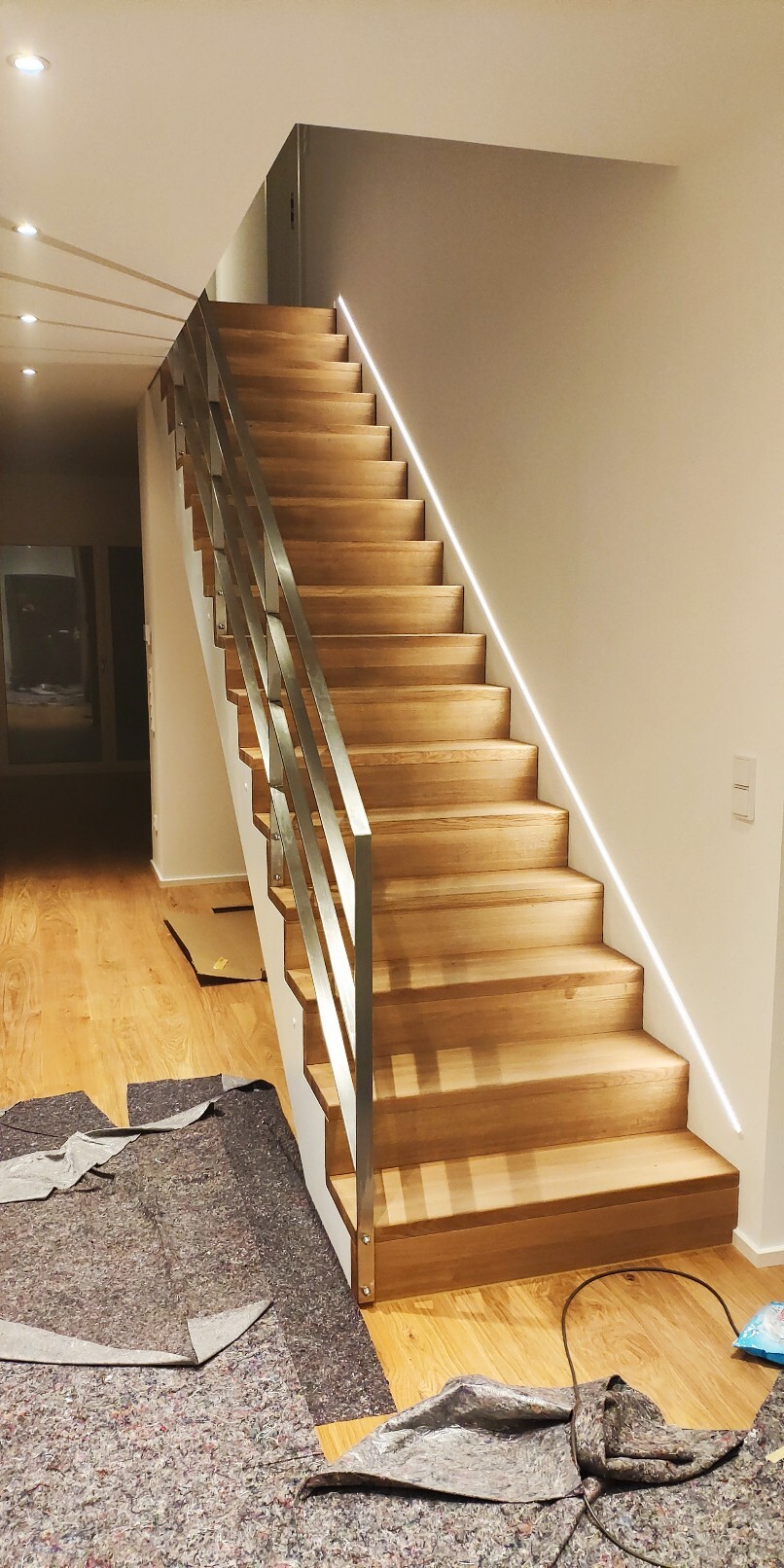 Moderne Holzstufen-Treppe mit Metallgeländer im Innenraum; Bauabfälle auf dem Boden.