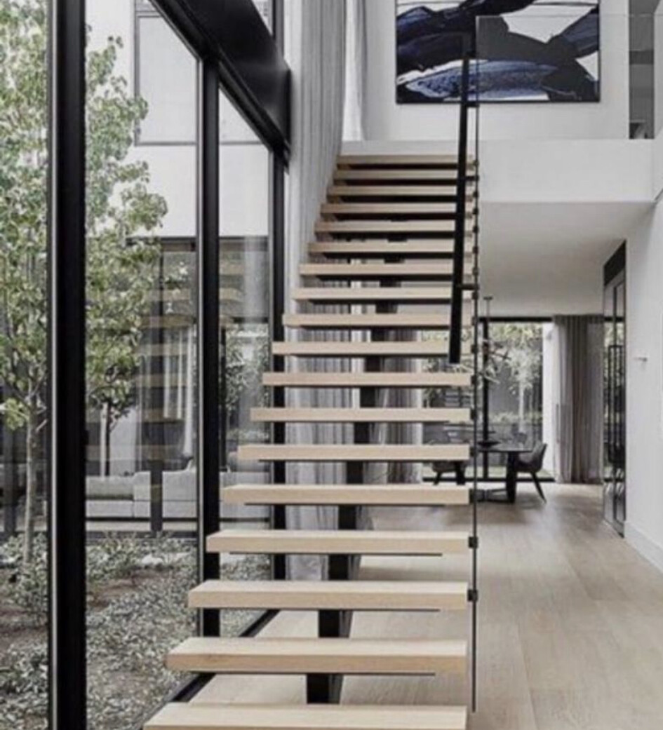Moderne offene Treppe aus Holzstufen mit Metallseilen neben Glaswand, Wohnzimmer im Hintergrund.