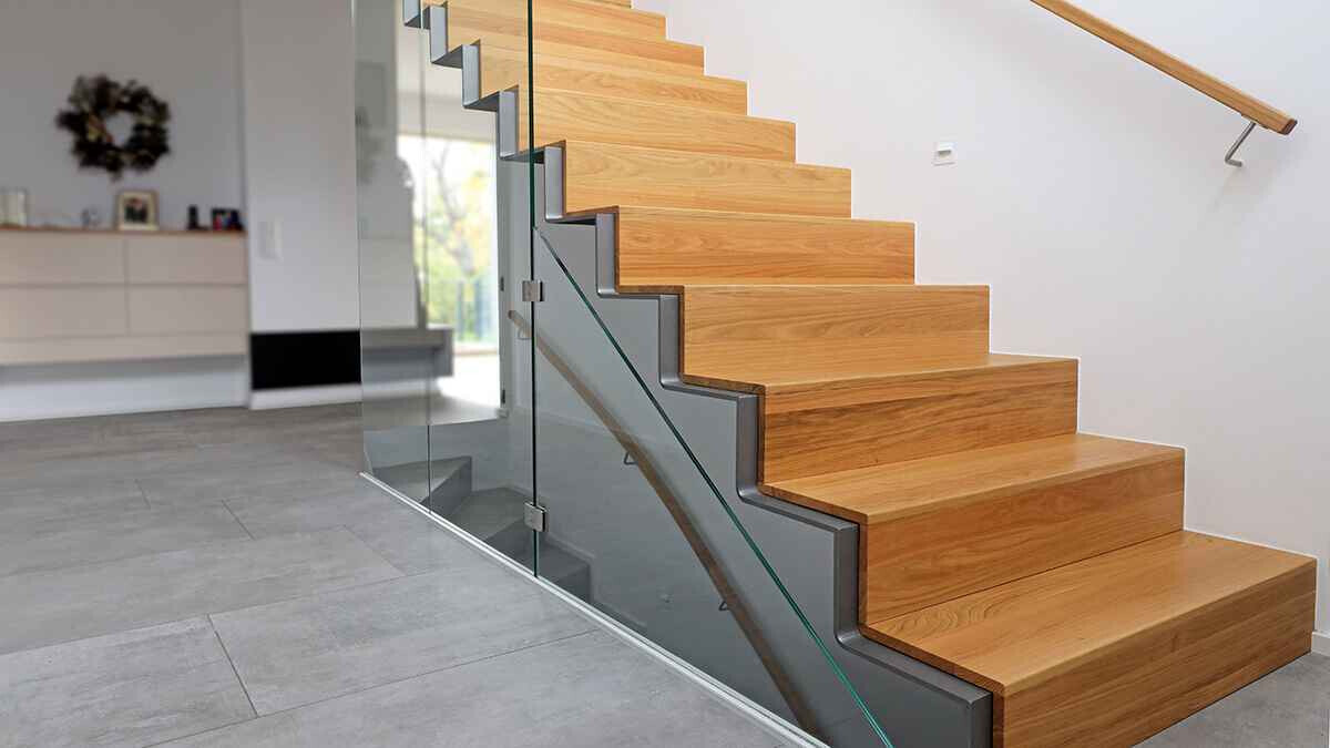 Moderne Holzstufen mit Glasgeländer, helle Innenwand und Fliesenboden.