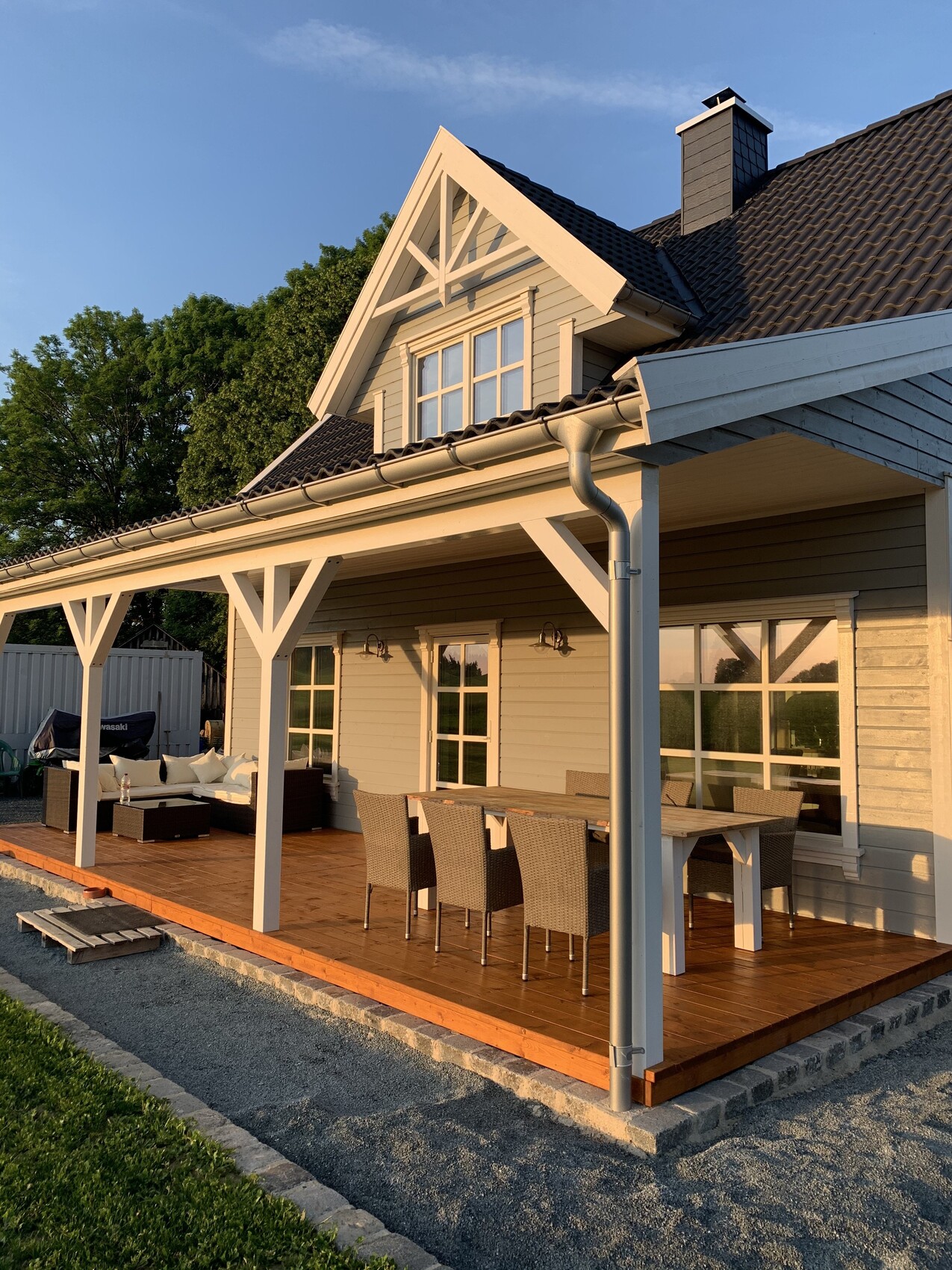 Holzveranda eines Hauses mit Esstisch und Stühlen, Lounge-Ecke, Dachgaube, Garten im Hintergrund