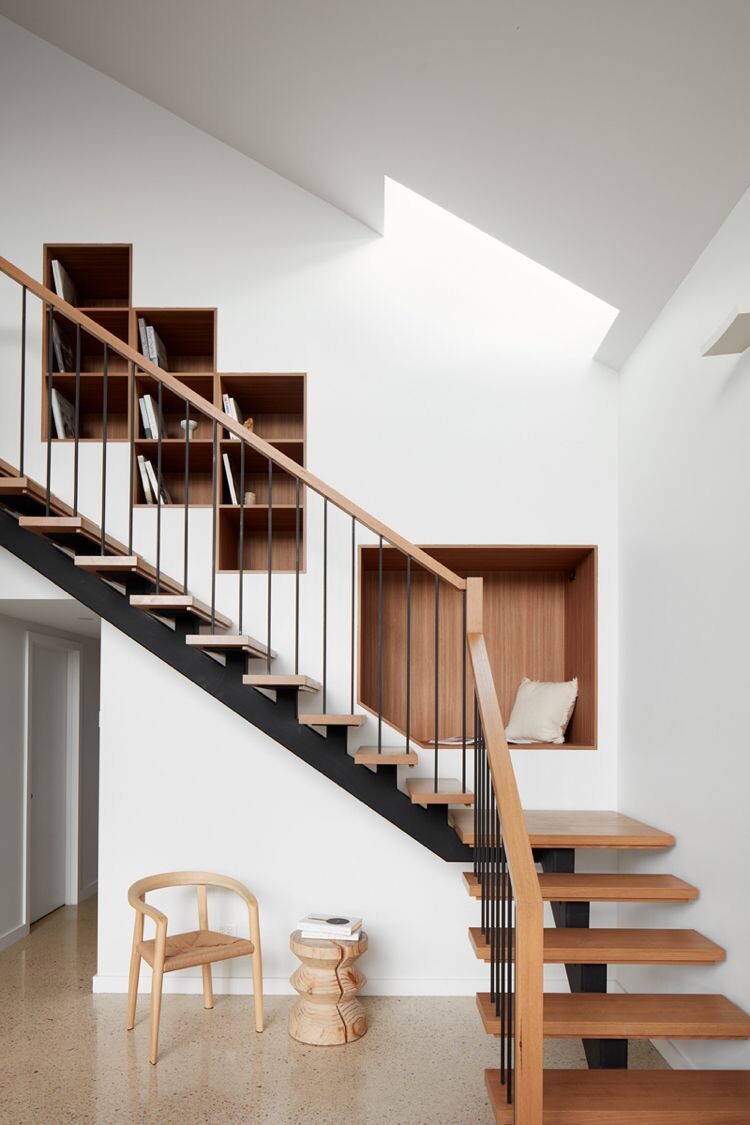 Moderne Holztreppe mit schwarzem Geländer, Wandregale, Nische mit Kissen, Holzstuhl, Dachlicht