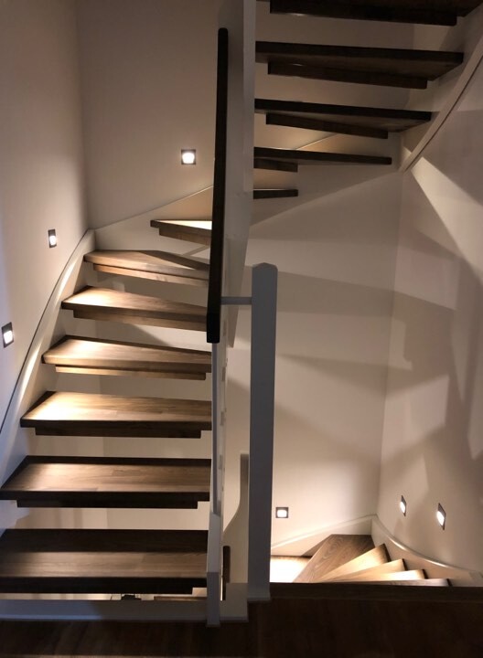 Moderne doppelte Holztreppe mit dunklen Stufen, weißem Geländer und Wandlichtern.